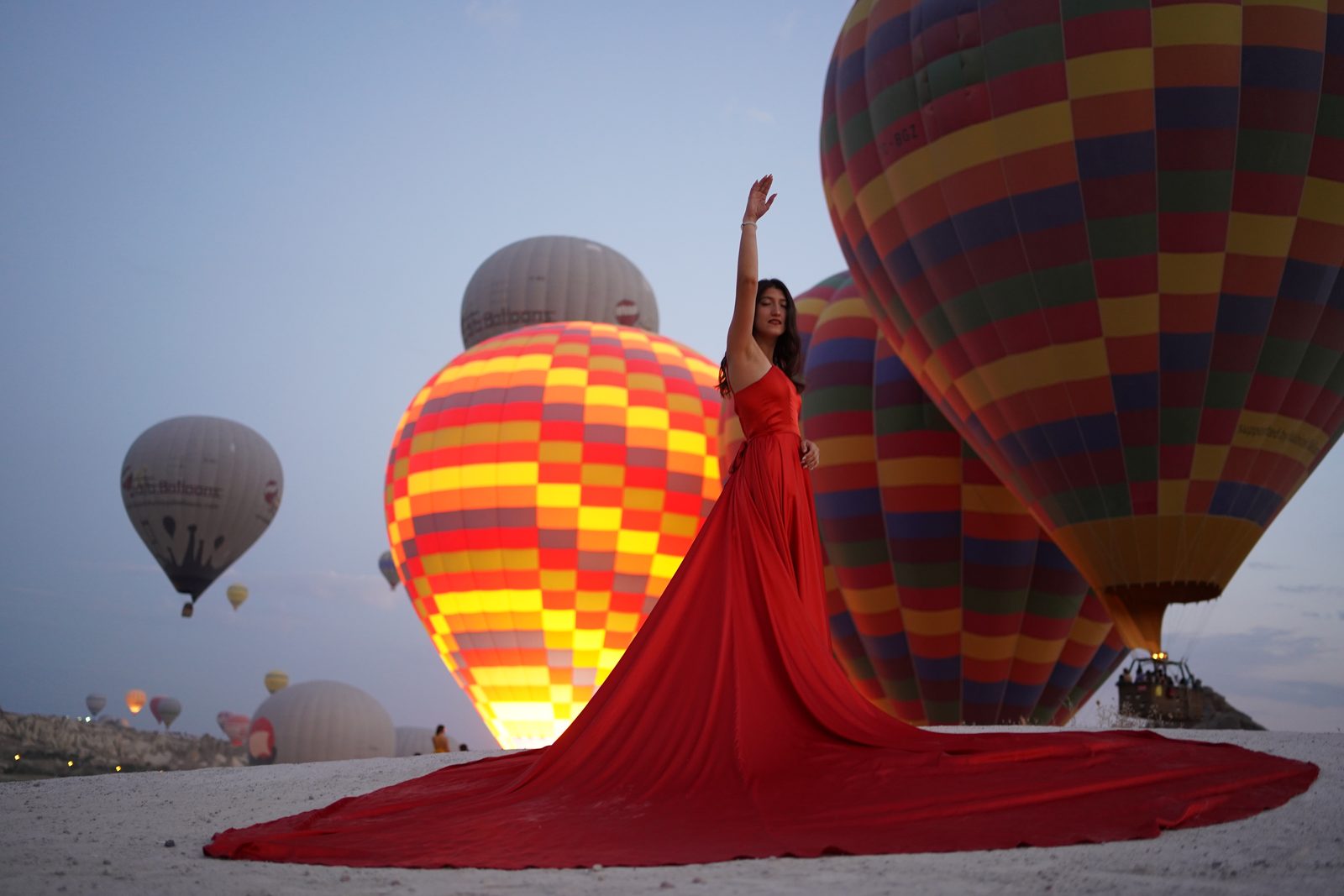 Our guest in a red dress raising her arm among Cappadocia balloons at dawn