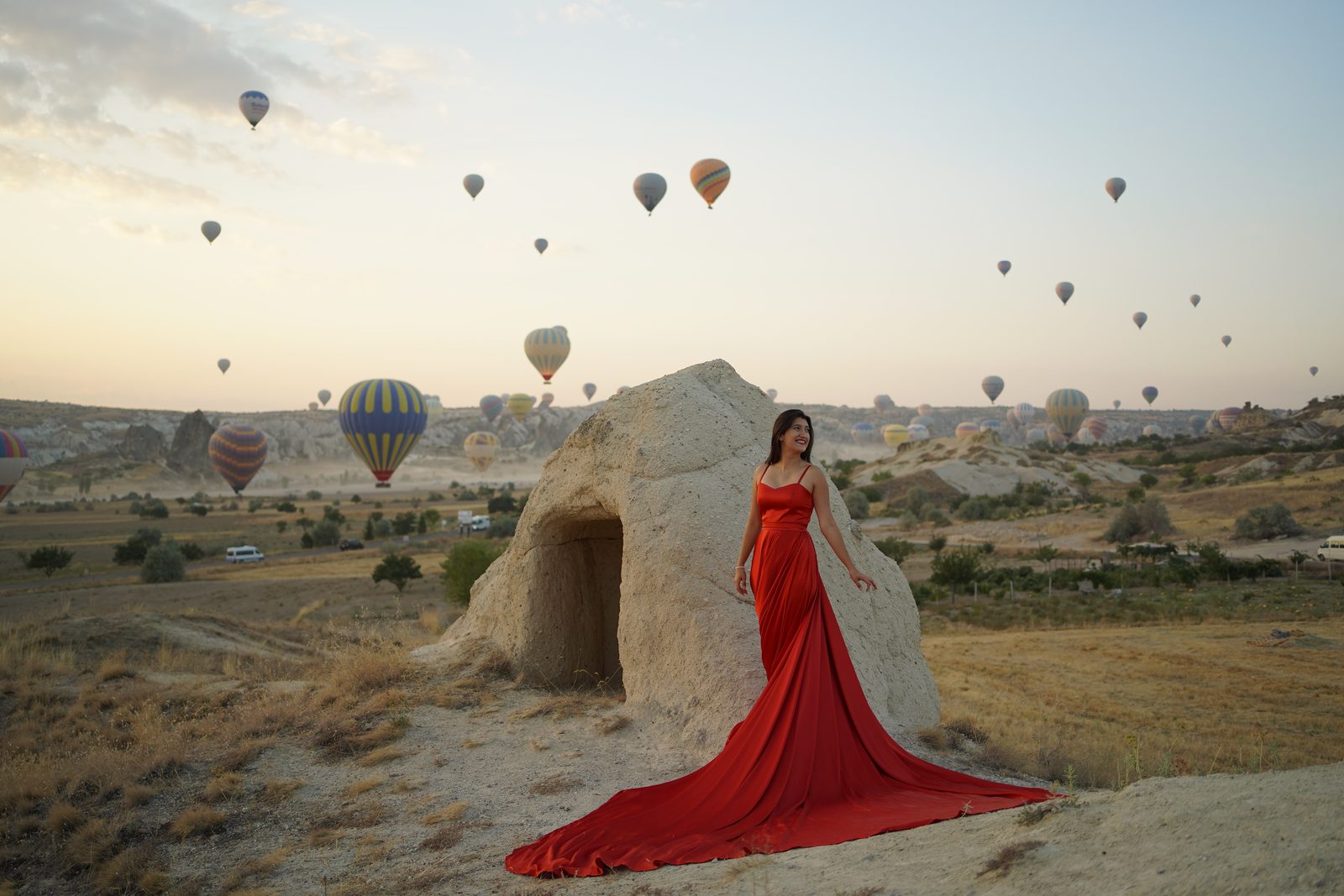 Our guest in a red dress with Cappadocia balloons at sunrise
